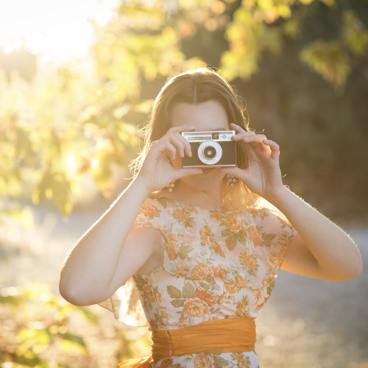 A photo of a girl covering her face with a camera during golden hour